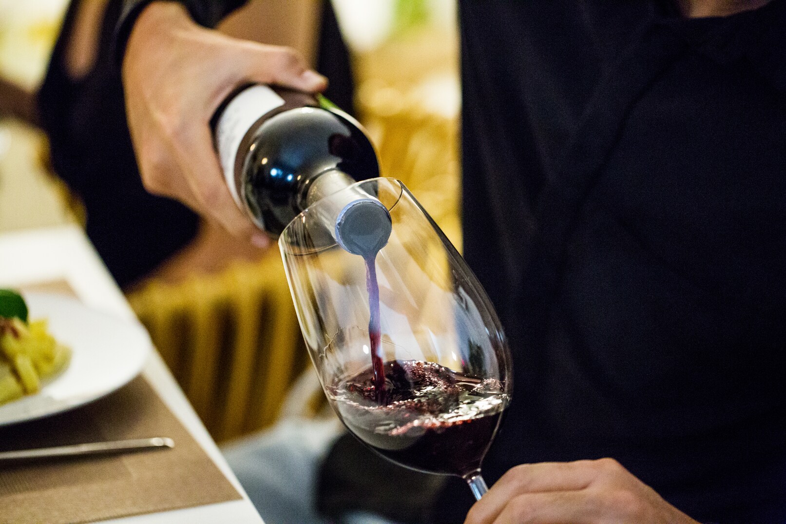 Midsection of man pouring red wine in glass during dinner party at home