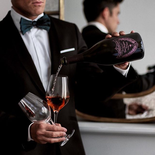 A man in a black suit pouring Dom Périgno into a wine glass