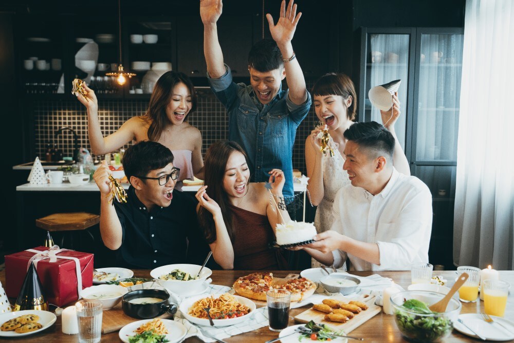 A group of friends celebrating a chinese party with raised hands and joyful expressions around a table full of food