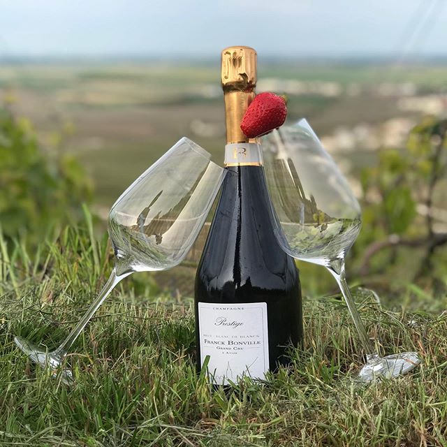 A  bottle of Franck Bonville 'Prestige' champagne placed on grass with two empty wine glasses crossed behind it