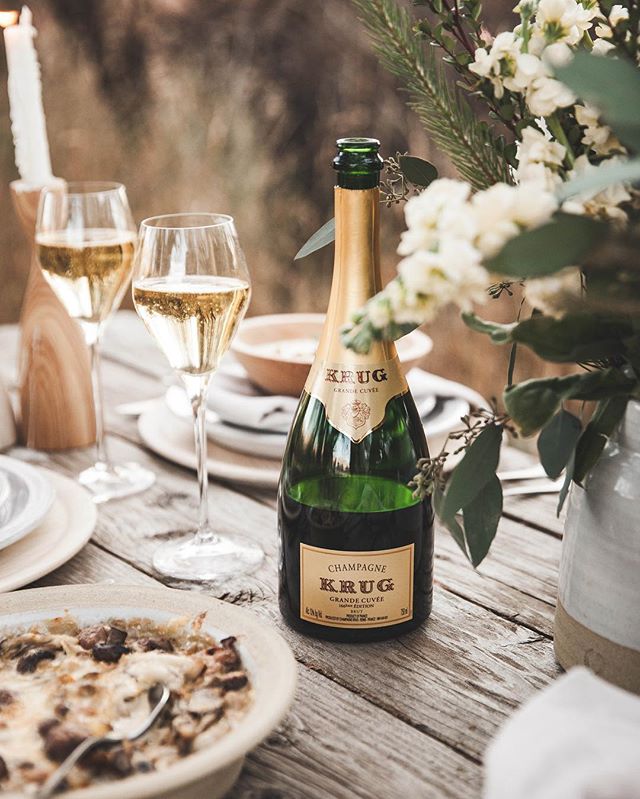 a rustic wooden table adorned with a bottle of Krug champagne, fluted glasses half-filled with bubbly champagne, and plates with slices of pizza