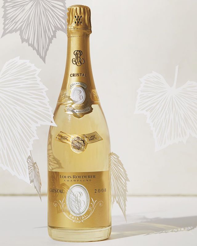 A bottle of Louis Roederer Cristal vintage champagne from 2008, placed against a plain background with white decorative leaves in relief