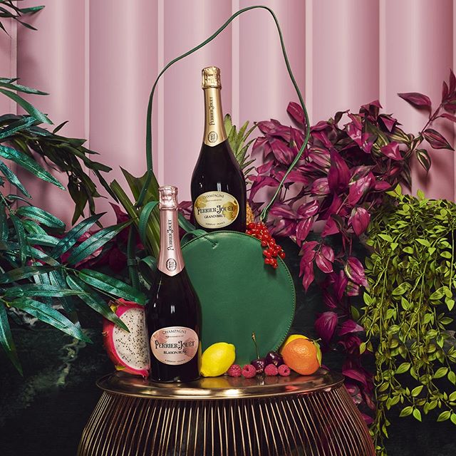 Two bottles of Perrier-Jouët champagne, one small and one large, against a backdrop of pink vertical stripes